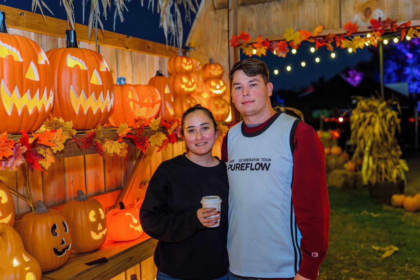 A couple smiling in front of a wall of glowing jack-o-lanterns