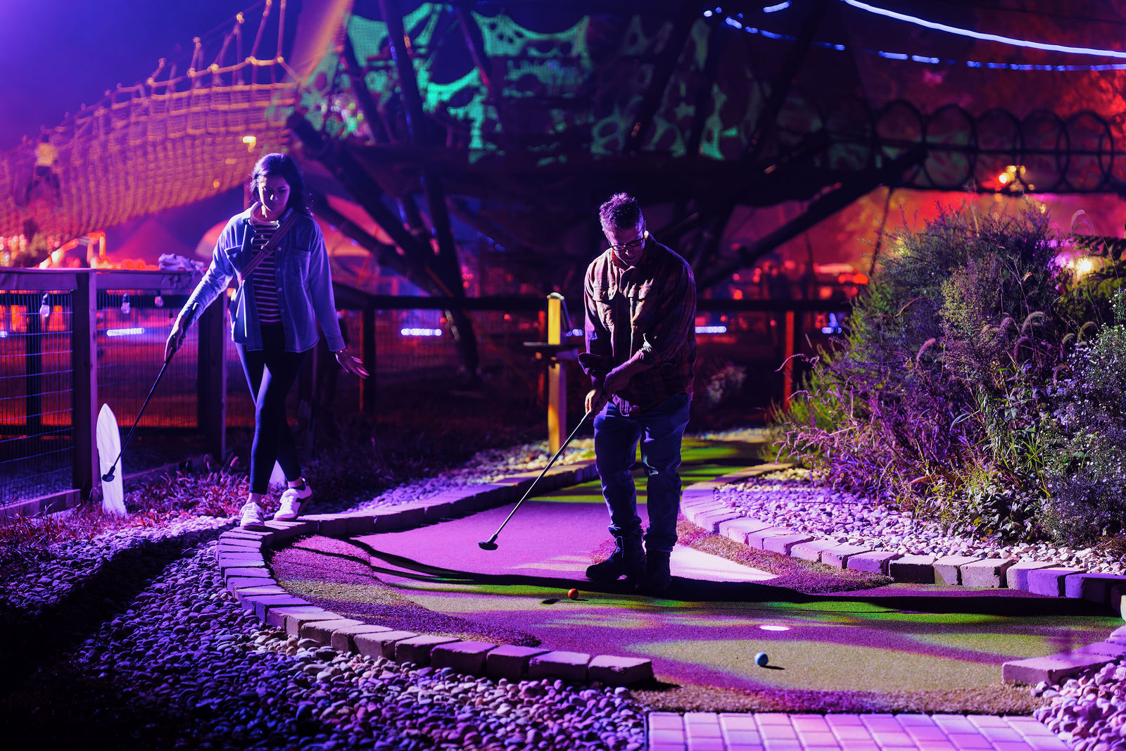 Guests playing graveyard mini golf at night under purple lights